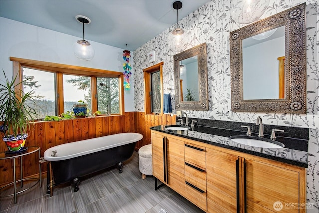 full bath with double vanity, a freestanding tub, a wainscoted wall, and a sink