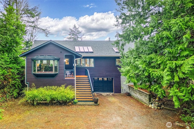 view of front of house with stairway, a shingled roof, a garage, dirt driveway, and roof mounted solar panels