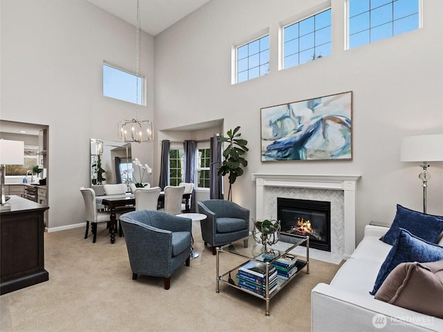 carpeted living room featuring baseboards, an inviting chandelier, and a high end fireplace