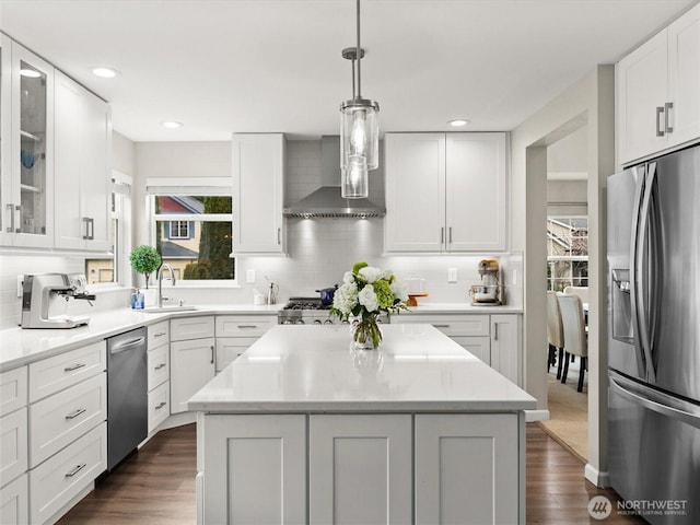 kitchen featuring a sink, wall chimney range hood, appliances with stainless steel finishes, white cabinetry, and dark wood-style flooring