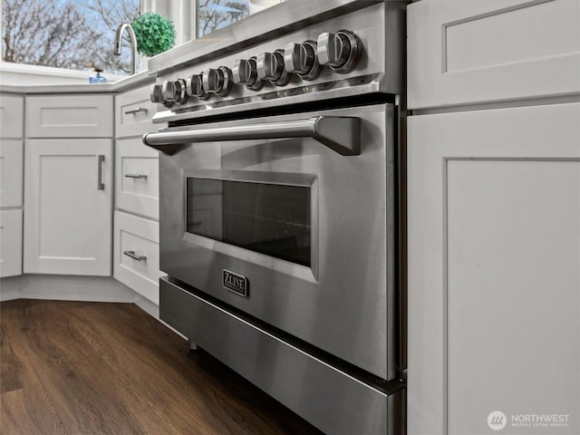 interior details featuring white cabinetry, stainless steel stove, light countertops, and dark wood-style flooring