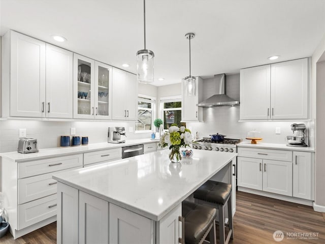 kitchen featuring stainless steel dishwasher, a center island, white cabinets, wall chimney range hood, and glass insert cabinets