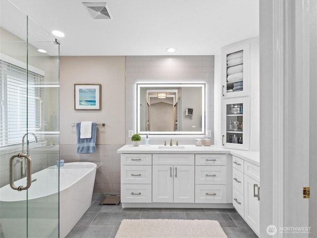 bathroom featuring tile patterned flooring, visible vents, a shower stall, tile walls, and vanity