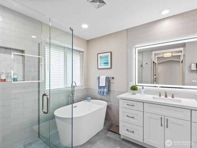 bathroom featuring vanity, visible vents, a stall shower, a freestanding bath, and tile walls