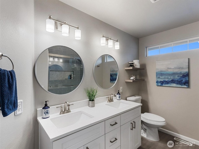 bathroom with double vanity, tiled shower, toilet, and a sink