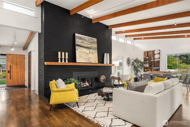 living area with beam ceiling, a high ceiling, a brick fireplace, and wood finished floors