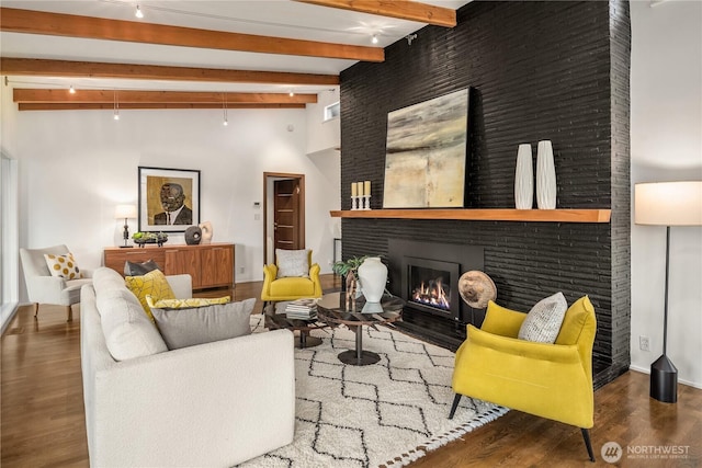 living room with beam ceiling, a high ceiling, a fireplace with flush hearth, and wood finished floors