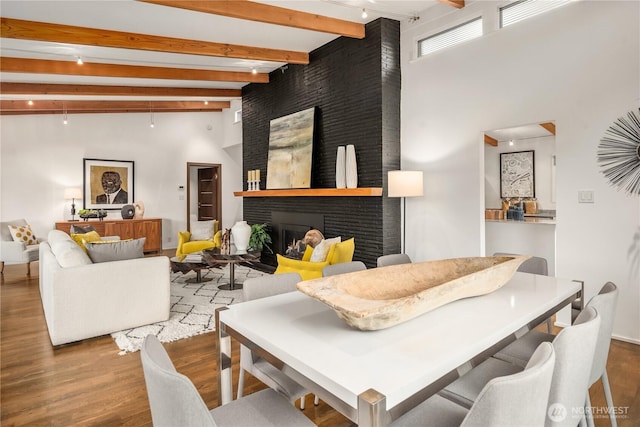 living room with beamed ceiling, a large fireplace, a towering ceiling, and wood finished floors