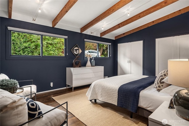 bedroom with lofted ceiling with beams, baseboards, wood finished floors, and track lighting