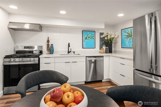 kitchen with a sink, dark wood-type flooring, appliances with stainless steel finishes, white cabinetry, and wall chimney range hood