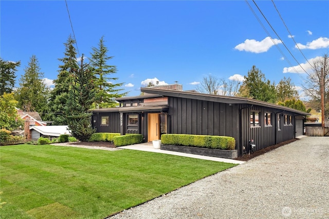 mid-century modern home with a front lawn, board and batten siding, and a chimney