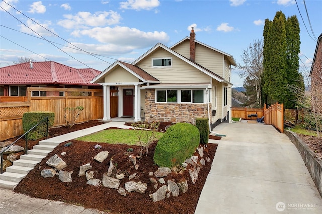 view of front facade featuring stone siding, concrete driveway, and fence