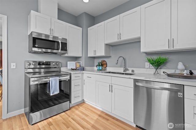 kitchen with a sink, light countertops, white cabinets, appliances with stainless steel finishes, and light wood-type flooring