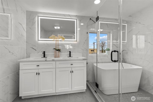 full bathroom featuring a sink, a soaking tub, tile walls, and double vanity