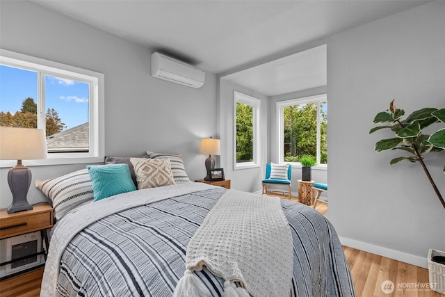 bedroom featuring baseboards, an AC wall unit, and wood finished floors