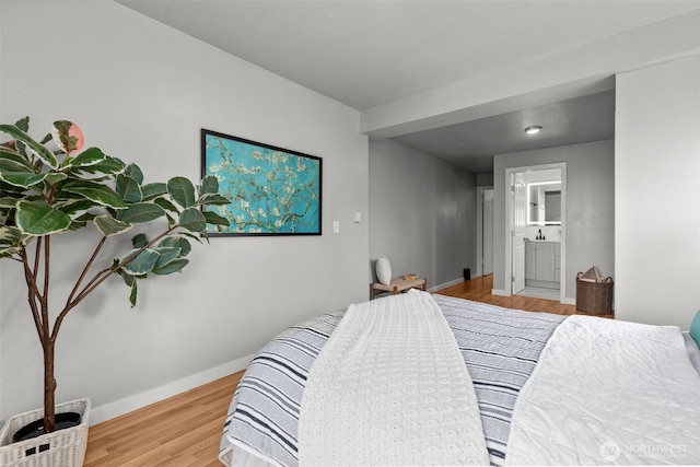 bedroom with connected bathroom, baseboards, and wood finished floors