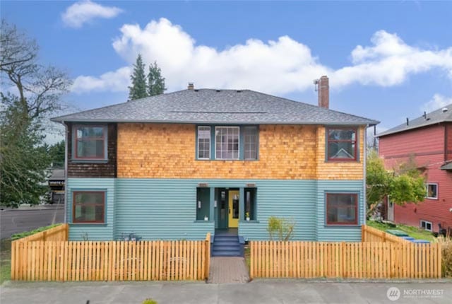 rear view of house with roof with shingles, a fenced front yard, and a chimney