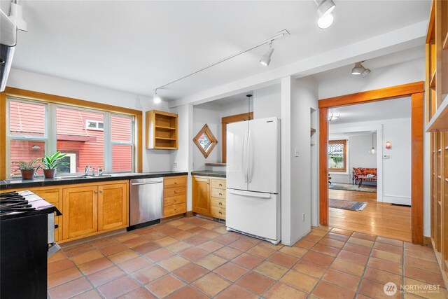 kitchen with dark countertops, range with gas stovetop, dishwasher, and freestanding refrigerator