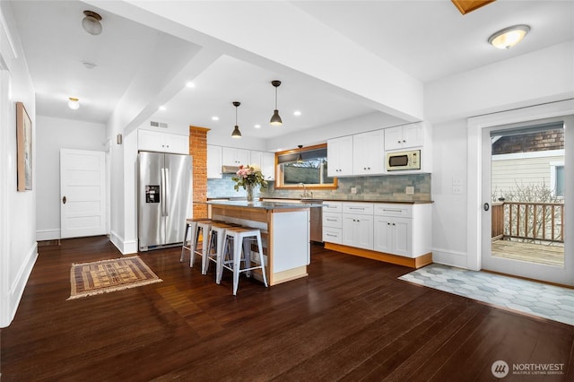 kitchen featuring dark wood-type flooring, stainless steel refrigerator with ice dispenser, a breakfast bar area, white cabinets, and white microwave