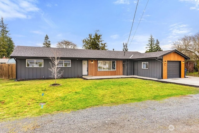 view of front facade with driveway, fence, board and batten siding, a front yard, and an attached garage