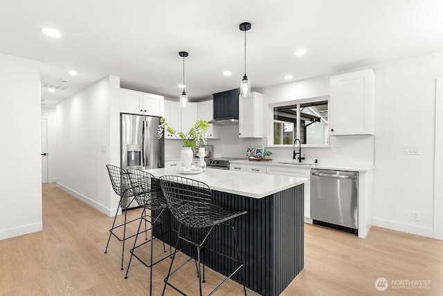 kitchen featuring a center island, a breakfast bar area, appliances with stainless steel finishes, light wood-style floors, and a sink