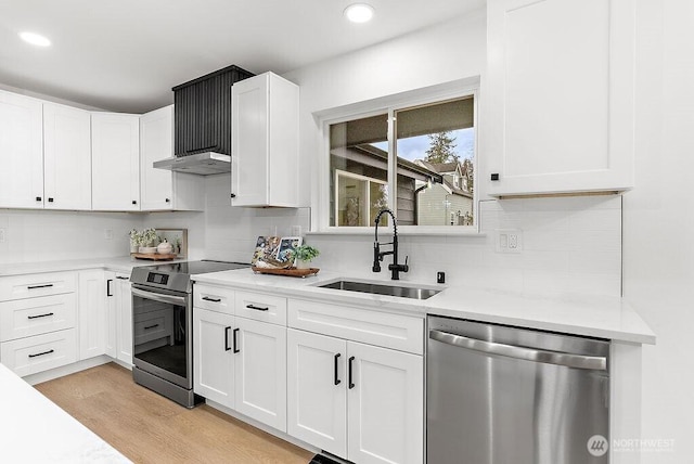 kitchen with light wood finished floors, decorative backsplash, appliances with stainless steel finishes, white cabinetry, and a sink