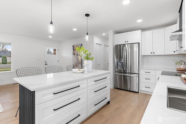 kitchen featuring light wood finished floors, tasteful backsplash, light stone countertops, stainless steel fridge with ice dispenser, and pendant lighting