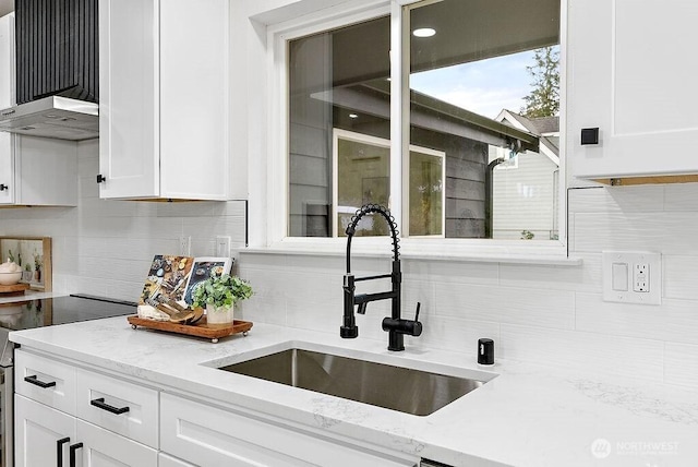 kitchen with a sink, under cabinet range hood, white cabinetry, decorative backsplash, and light stone countertops