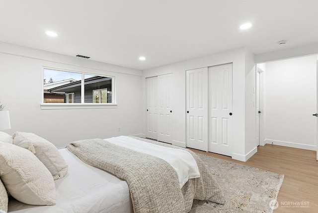 bedroom featuring visible vents, baseboards, multiple closets, recessed lighting, and wood finished floors