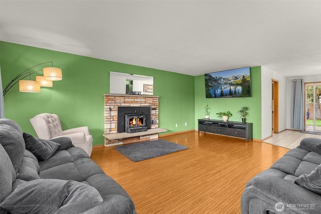 living area with a fireplace, an accent wall, baseboards, and wood finished floors