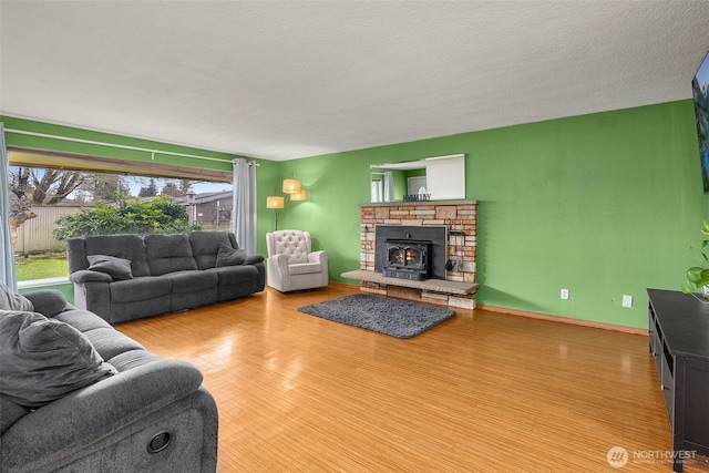 living room featuring a stone fireplace, a textured ceiling, baseboards, and wood finished floors