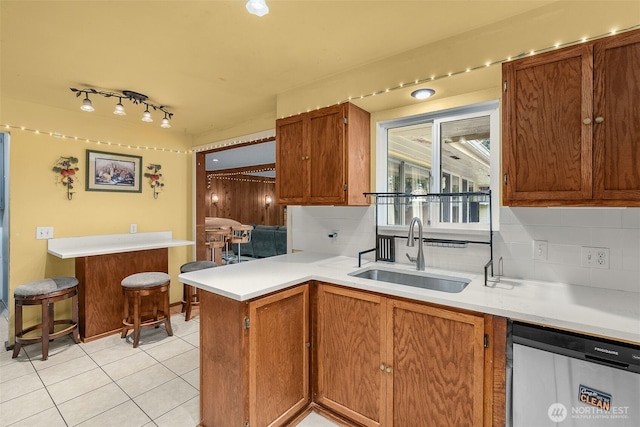 kitchen with a sink, a peninsula, decorative backsplash, and stainless steel dishwasher