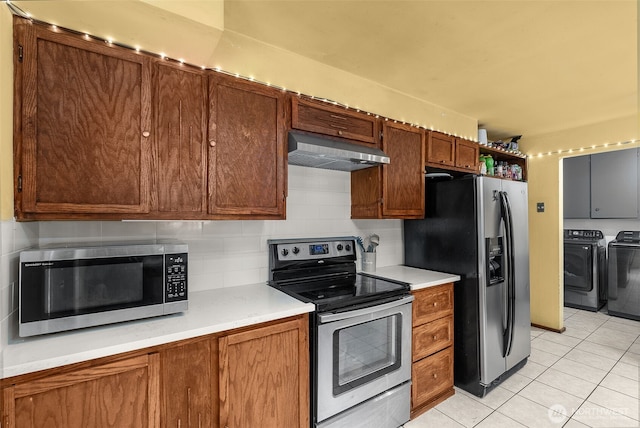 kitchen with independent washer and dryer, stainless steel appliances, light countertops, under cabinet range hood, and tasteful backsplash