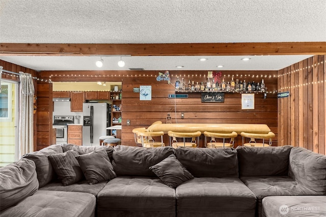 living room featuring beam ceiling, wood walls, and a dry bar