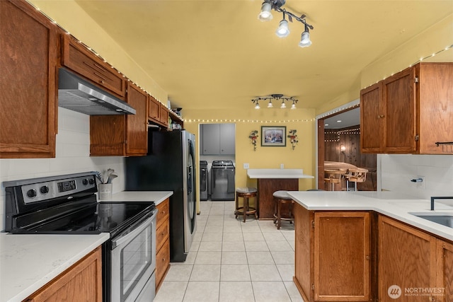 kitchen featuring light countertops, light tile patterned floors, appliances with stainless steel finishes, independent washer and dryer, and wall chimney exhaust hood