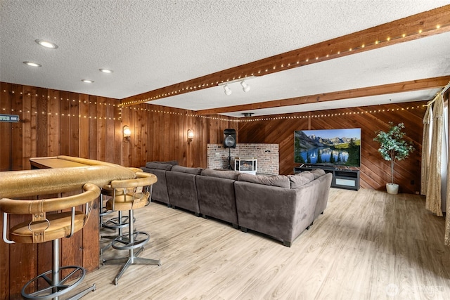 living room with beam ceiling, wooden walls, light wood-type flooring, and a textured ceiling