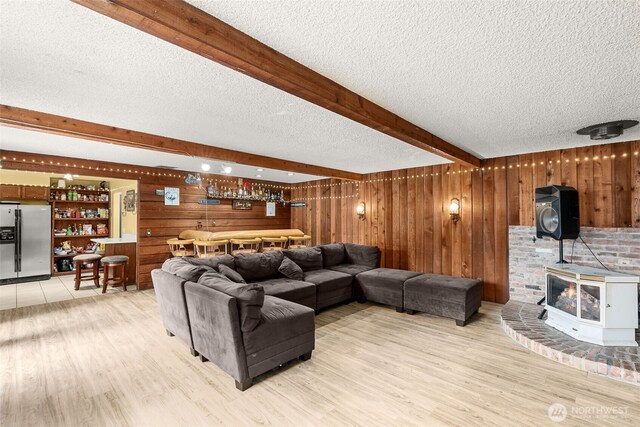 living area featuring light wood-type flooring, beam ceiling, a textured ceiling, wooden walls, and a bar