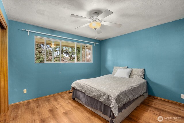 bedroom featuring ceiling fan, wood finished floors, baseboards, and a textured ceiling