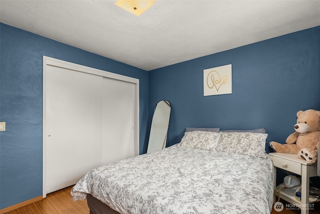 bedroom featuring a closet, baseboards, a textured wall, and wood finished floors