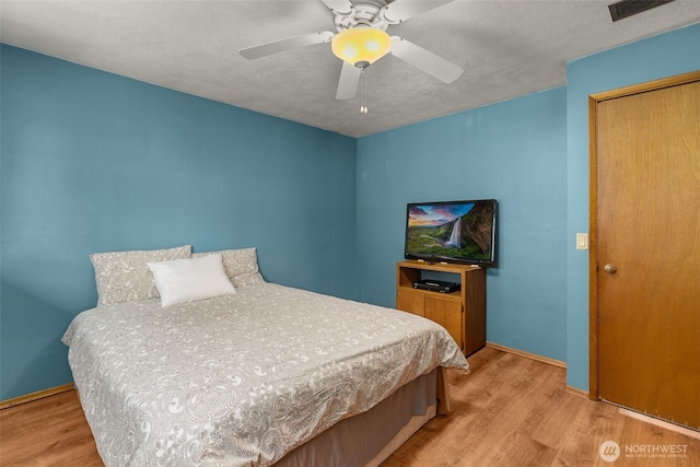 bedroom featuring light wood finished floors, visible vents, a textured ceiling, and ceiling fan