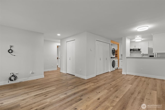 unfurnished living room with baseboards, light wood-style flooring, and stacked washing maching and dryer