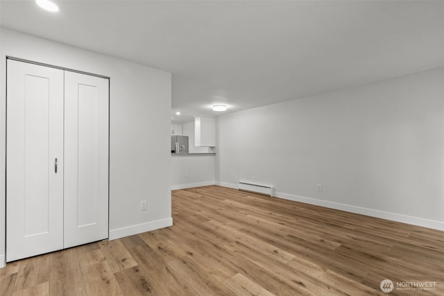 unfurnished bedroom featuring baseboards, light wood-type flooring, a closet, stainless steel fridge, and baseboard heating