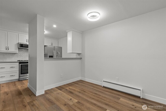 kitchen with backsplash, wood finished floors, stainless steel appliances, white cabinets, and a baseboard radiator