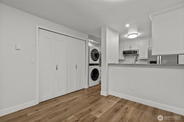 laundry area featuring baseboards, laundry area, a sink, stacked washer / dryer, and light wood-type flooring