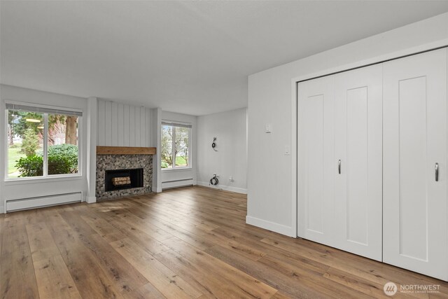 unfurnished living room featuring light wood finished floors, baseboard heating, a fireplace, and baseboards