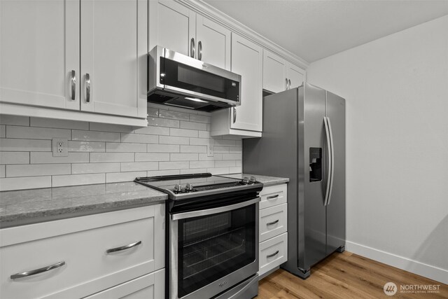 kitchen with tasteful backsplash, light stone counters, light wood-style flooring, appliances with stainless steel finishes, and white cabinets