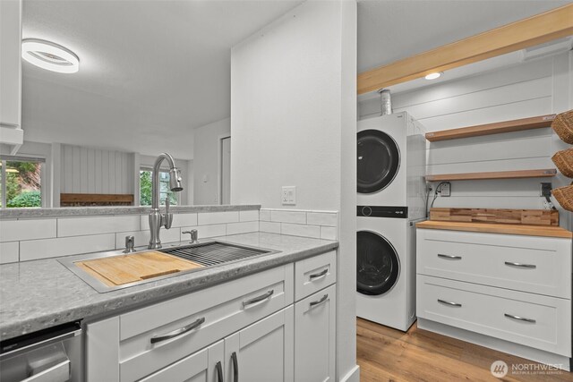 laundry room with a sink, laundry area, light wood-style floors, and stacked washing maching and dryer