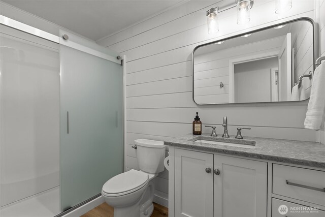 bathroom featuring vanity, toilet, a stall shower, and wood walls