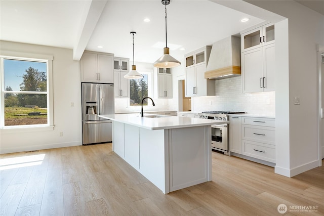 kitchen with a center island with sink, premium range hood, light wood-style flooring, light countertops, and premium appliances