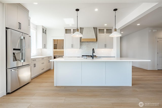 kitchen with a sink, wall chimney range hood, high end refrigerator, light wood finished floors, and light countertops